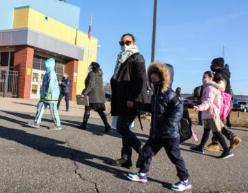 A parent holds their child's hand as they walk to school