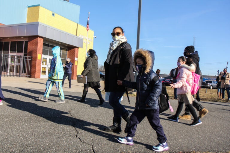 A parent holds their child's hand as they walk to school