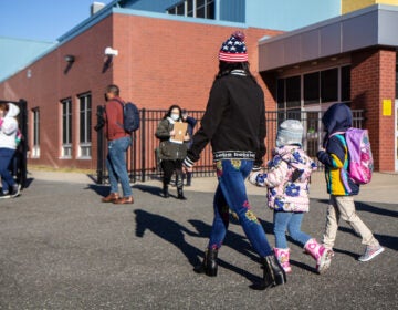 A parent holds their child's hand as they walk to school