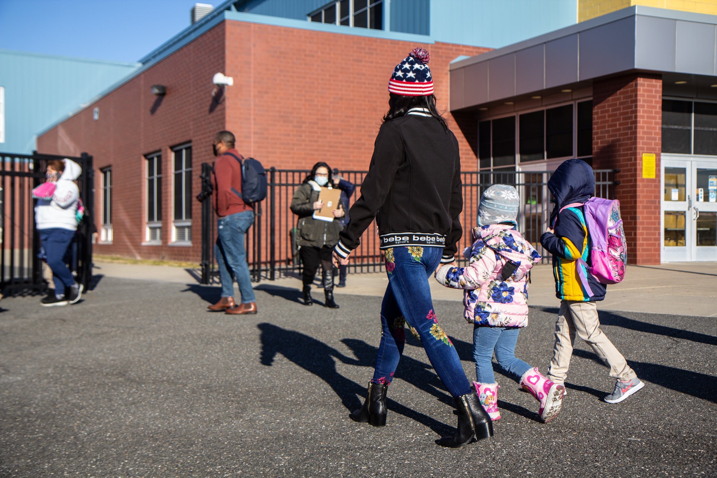 A parent holds their child's hand as they walk to school