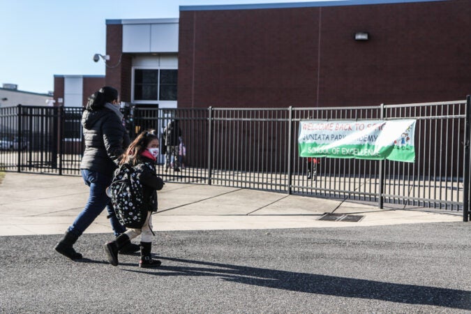 A parent holds their child's hand as they walk to school