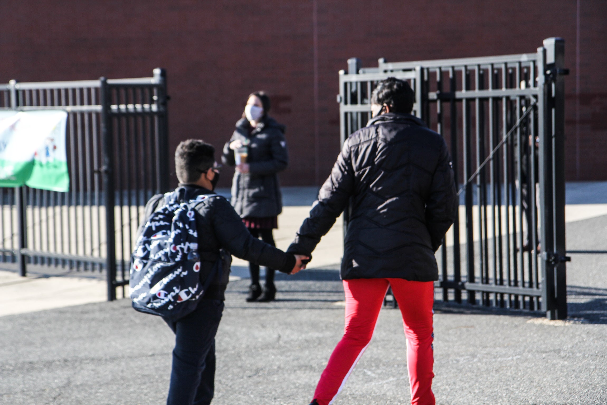 A parent holds their child's hand as they walk to school