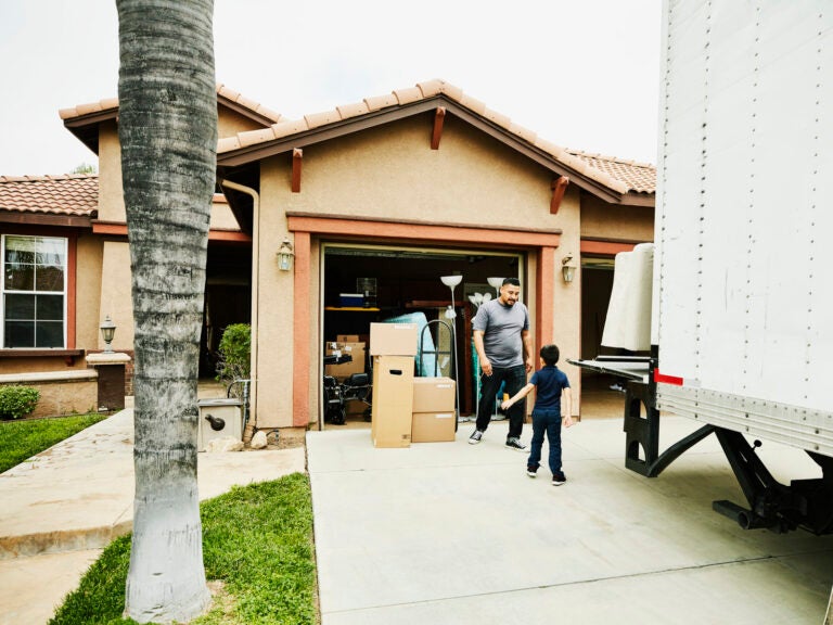 Young son helping father move items from moving truck into new house