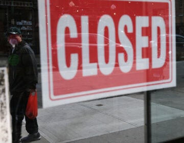 A person's reflection is seen in a store window that has a closed sign affixed to it