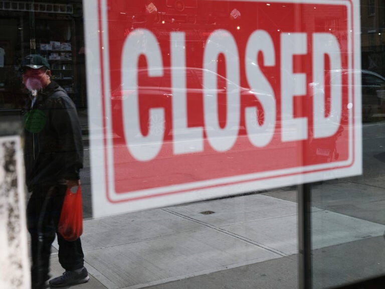 A person's reflection is seen in a store window that has a closed sign affixed to it