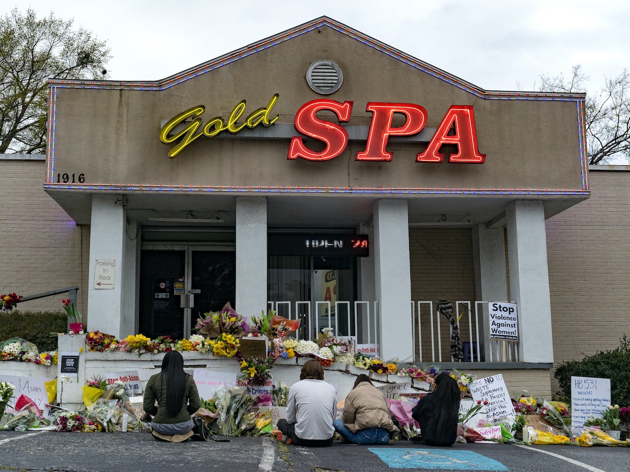 Mourners sit outside Gold Spa, where dozens have left bouquets and candles in the days since Tuesday's shootings.