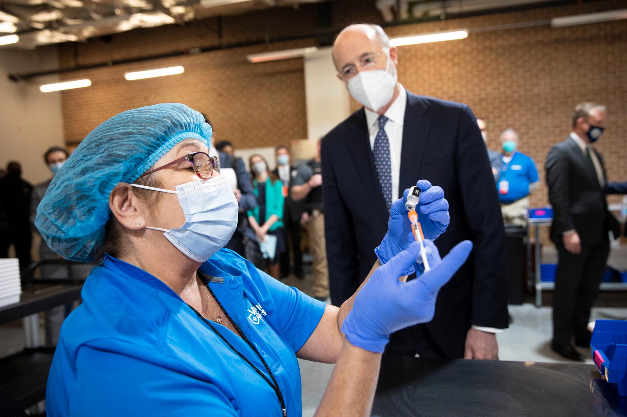 A health worker prepares a vile with COVID-19 vaccine as Pennsylvania Gov. Tom Wolf observes.