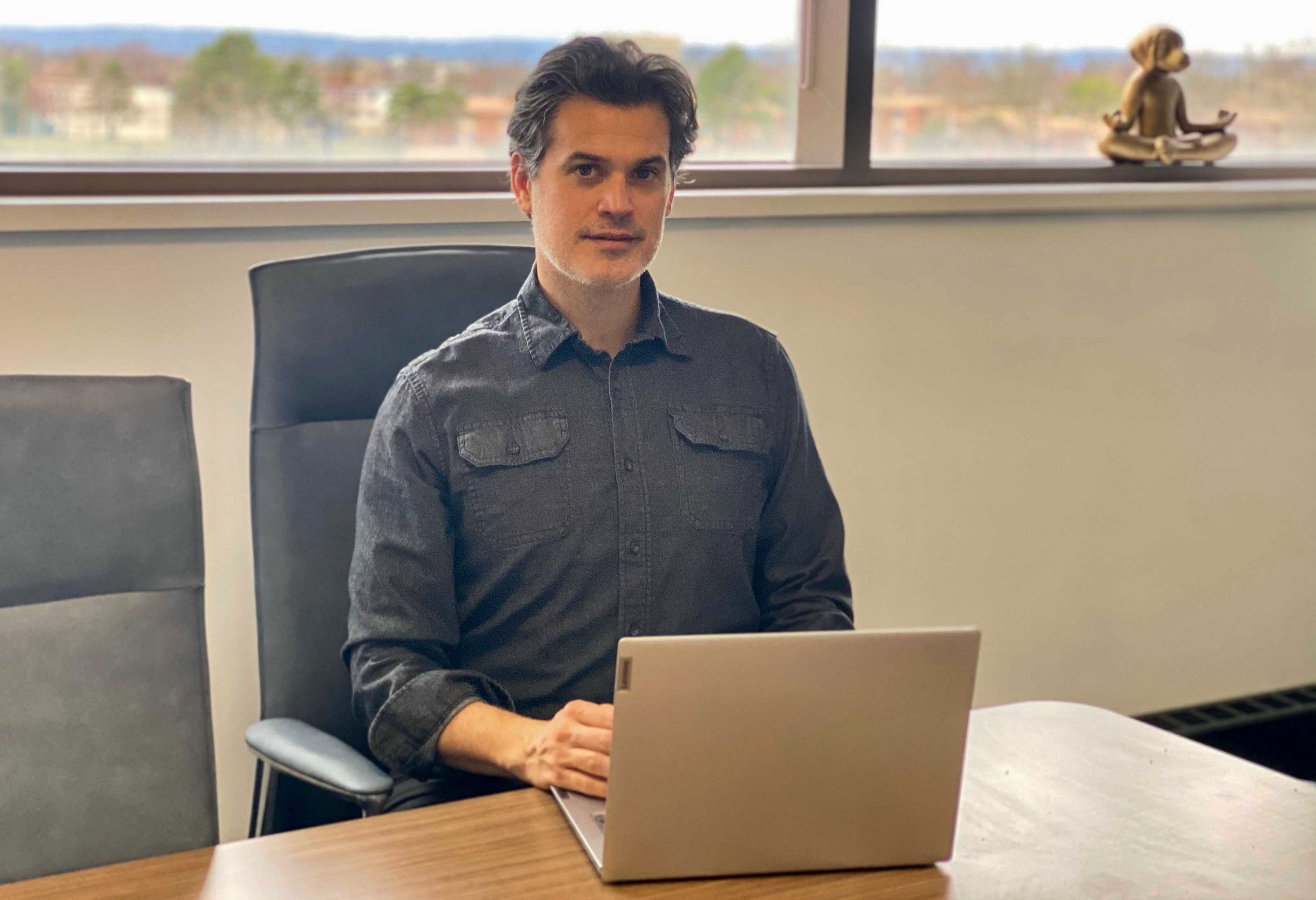 Psychologist Peter Economou sits at a desk with his laptop