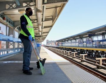 A SEPTA employee has a broom in hand at an outdoor station on the Market-Frankford line.