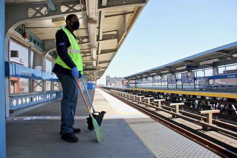 A SEPTA employee has a broom in hand at an outdoor station on the Market-Frankford line.