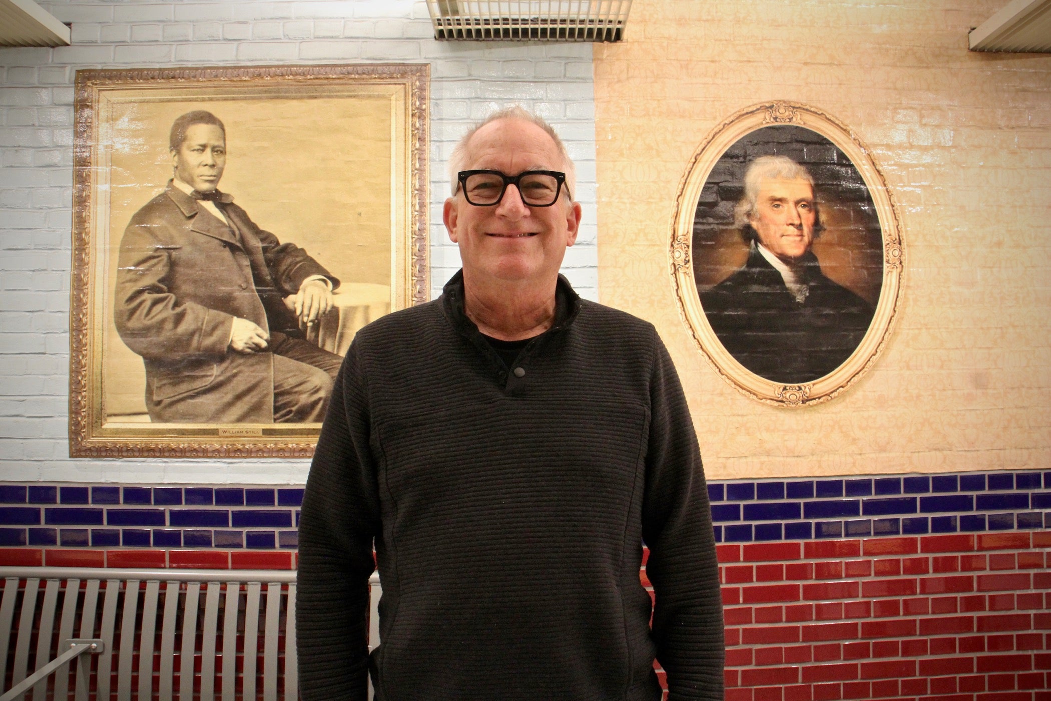 Artist Tom Judd created the murals for the Independence Hall SEPTA Station. He stands between portraits of abolitionist William Still and founding father Thomas Jefferson. (Emma Lee/WHYY)
