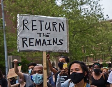 Protesters march outside Penn Museum, with one sign prominent that reads, 