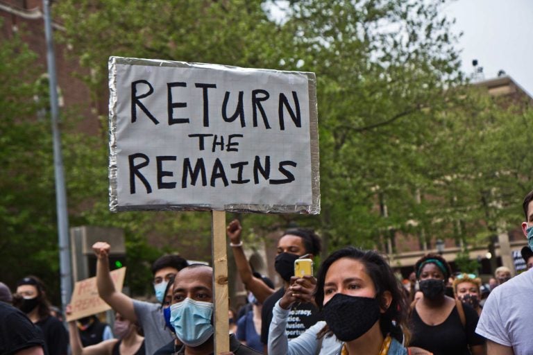 Protesters march outside Penn Museum, with one sign prominent that reads, 