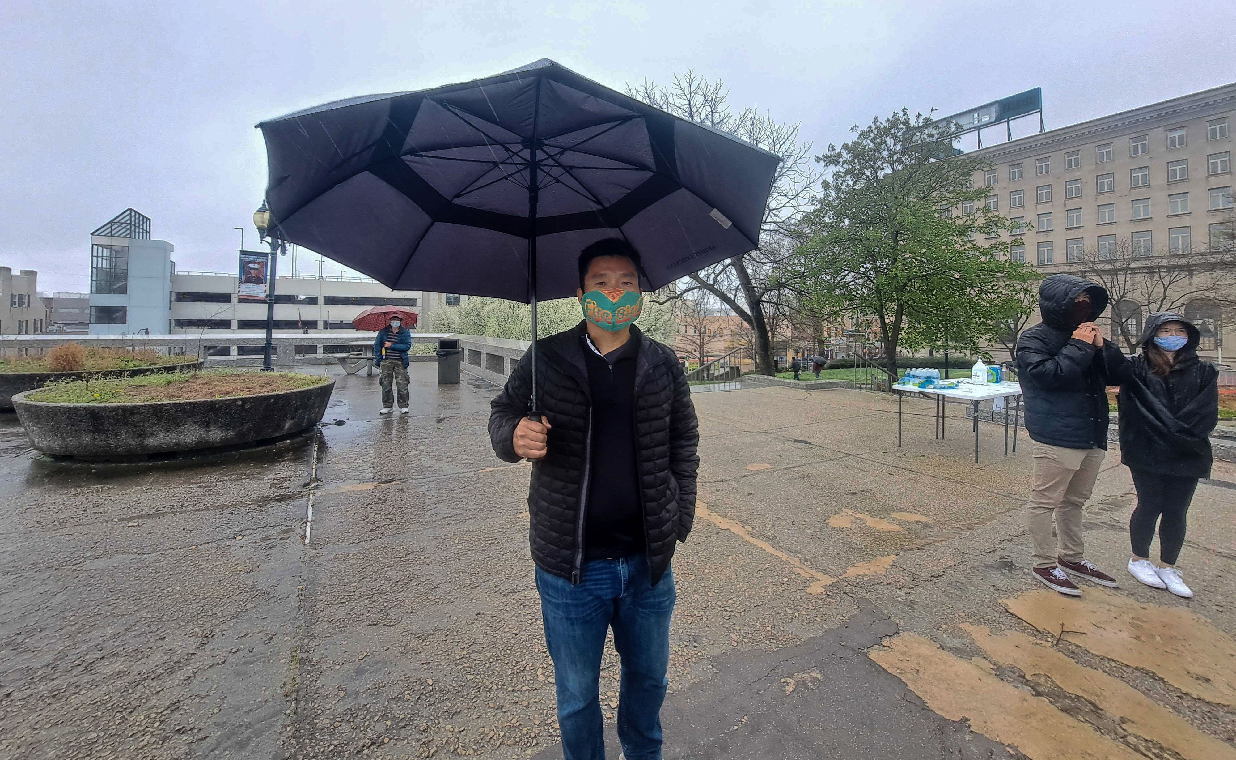 James Kim holds an umbrella while wearing a face mask