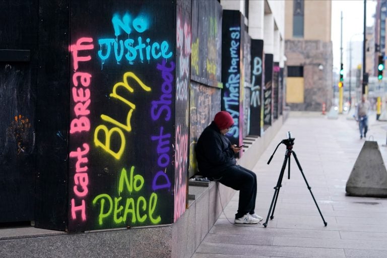 A person videotapes across the street from the Hennepin County Government Center, Thursday, April 8, 2021, in Minneapolis where testimony continues in the trial of former Minneapolis police officer Derek Chauvin. (AP Photo/Jim Mone)