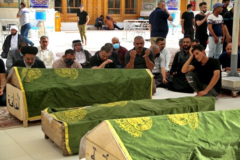 Mourners pray near the coffins of coronavirus patients killed in a hospital fire during their funeral at the Imam Ali shrin
