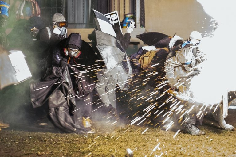 Demonstrators take cover from crowd-dispersal munitions from police outside the Brooklyn Center Police Department to protest the shooting death of Daunte Wright, Tuesday, April 13, 2021, in Brooklyn Center, Minn. (AP Photo/John Minchillo)