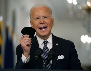 President Joe Biden holds a mask in his hand as he speaks from a podium