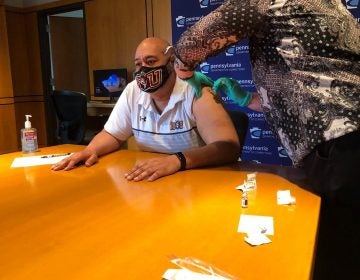 A person receives the COVID-19 vaccine while sitting at a large table