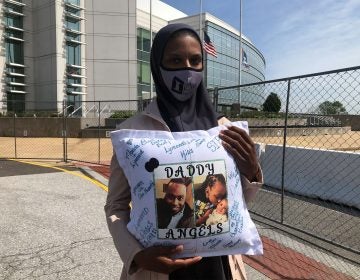 Amanda Spence holds a pillow with photos of her slain husband Lymond Moses and their two children in front of New Castle County police headquarters. (Cris Barrish/WHYY)