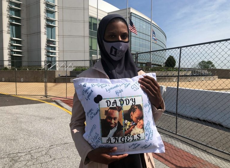Amanda Spence holds a pillow with photos of her slain husband Lymond Moses and their two children in front of New Castle County police headquarters. (Cris Barrish/WHYY)