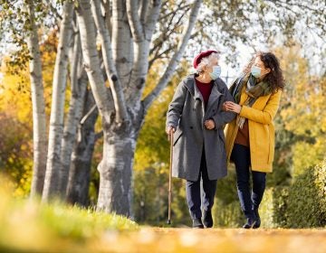 Granddaughter walking with senior woman in park wearing face mask for safety against covid-19