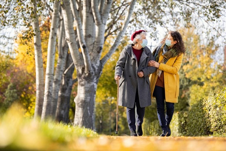 Granddaughter walking with senior woman in park wearing face mask for safety against covid-19