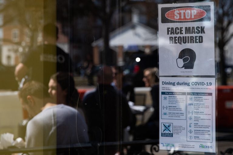 A sign requiring face masks and COVID-19 protocols is displayed at a restaurant in Plymouth, Mich., on March 21. Coronavirus cases in Michigan are skyrocketing after months of steep declines, one sign that a new surge may be starting. (Emily Elconin/Bloomberg via Getty Images)