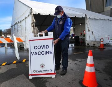 A health worker stands next to a COVID-19 vaccine sign