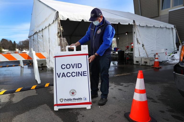A health worker stands next to a COVID-19 vaccine sign