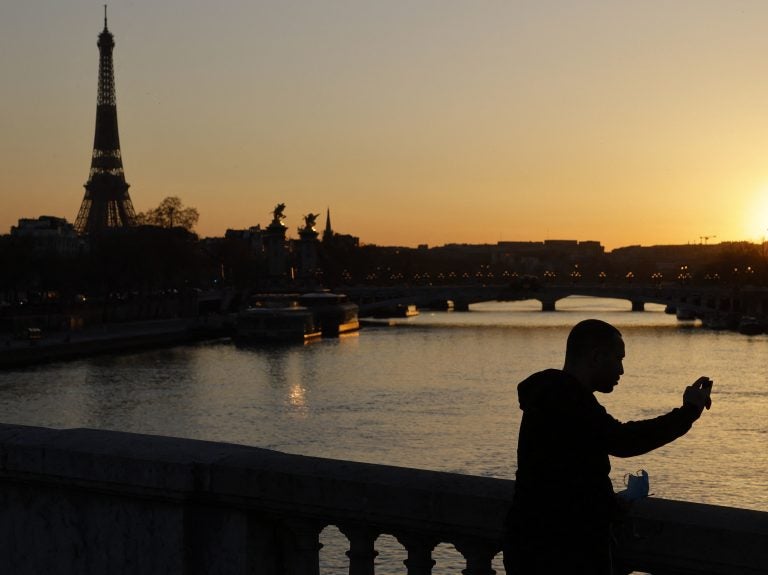 A man takes a picture with mobile phone at the sunset with Eiffel Tower in the background