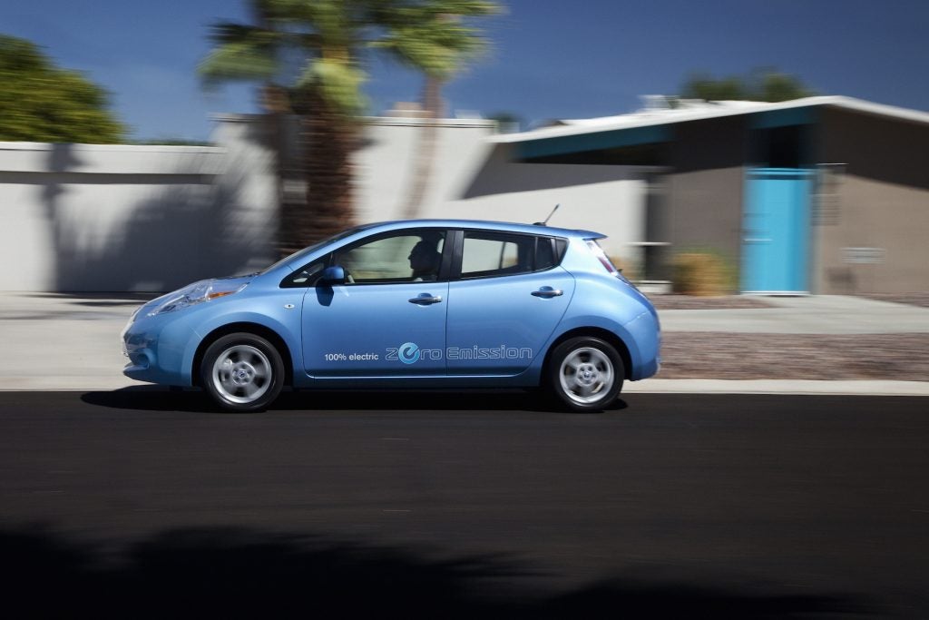 A blue 2012 Nissan Leaf drives on the road.