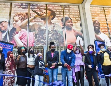 Mural artist Russell Craig cuts the ribbon on the West side of Philadelphia’s Municipal Services Building at the dedication of the Crown mural on May 11, 2021. (Kimberly Paynter/WHYY)