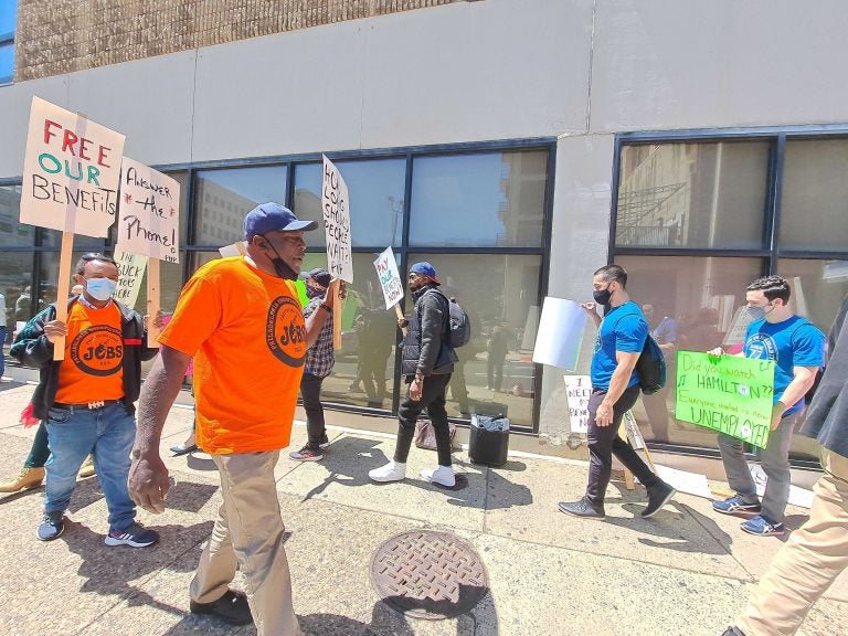 People, some holding signs, participate in a protest demanding Pa. pay out their unemployment benefits