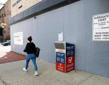In this July 1, 2020, file photo, a woman walks past a vote-by-mail drop box for the upcoming New Jersey primary election outside the Camden, N.J., Administration Building. (AP Photo/Matt Slocum)