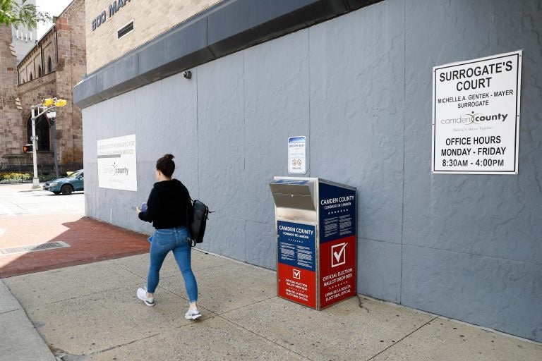 In this July 1, 2020, file photo, a woman walks past a vote-by-mail drop box for the upcoming New Jersey primary election outside the Camden, N.J., Administration Building. (AP Photo/Matt Slocum)