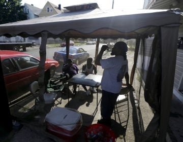 FILE - In this Wednesday, July 4, 2012 file photo, Dave Bailey, right, gulps water from a bottle while hanging inside of a tent on the sidewalk with his sons Daquan Bailey, 14, left, and Davandre Bailey, 17, while beating the heat on Fourth of July in Paterson, N.J. According to a study published Tuesday, May 25, 2021 in Nature Communications, during the summer of 2017 in nearly all large urban areas, people of color are exposed to more extreme urban heat than white people. (AP Photo/Julio Cortez, File)