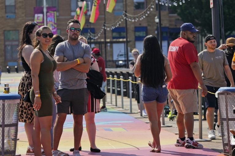 People, some with masks and some without, wait in line to be seated outdoors on a pier