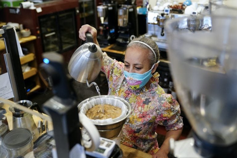 Edna Cruz makes coffee while wearing a mask inside her cafe