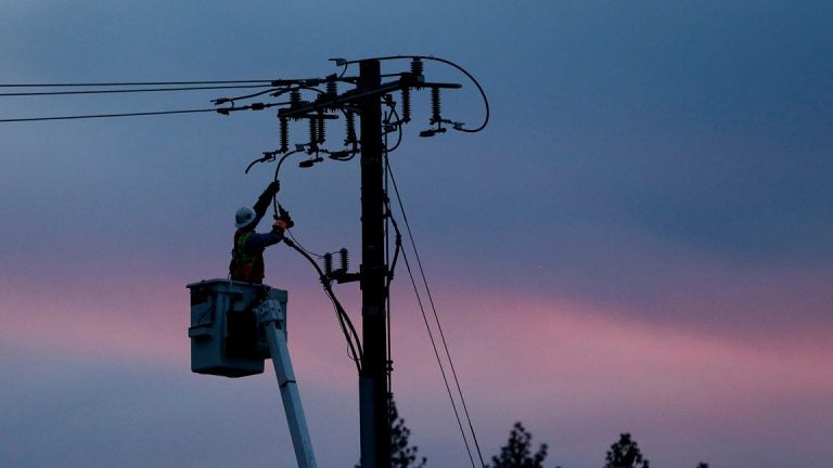A utility crew member works the lines against a cotton candy sky