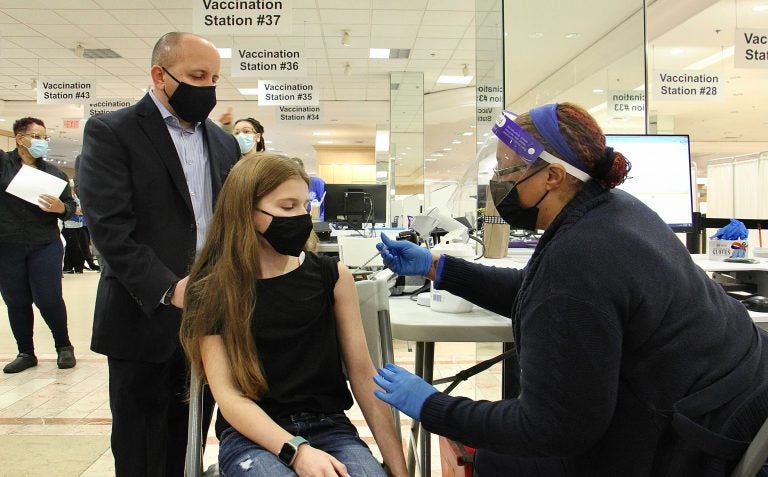 Jenna Baron, 12, of Voorhees, N.J., gets her first Pfizer COVID-19 shot from registered nurse Samantha Hickson at the Burlington County mega site in Moorestown. She is accompanied by her father, Robert Baron, a Vice President of operations for Virtua Medical Group. (Emma Lee/WHYY)
