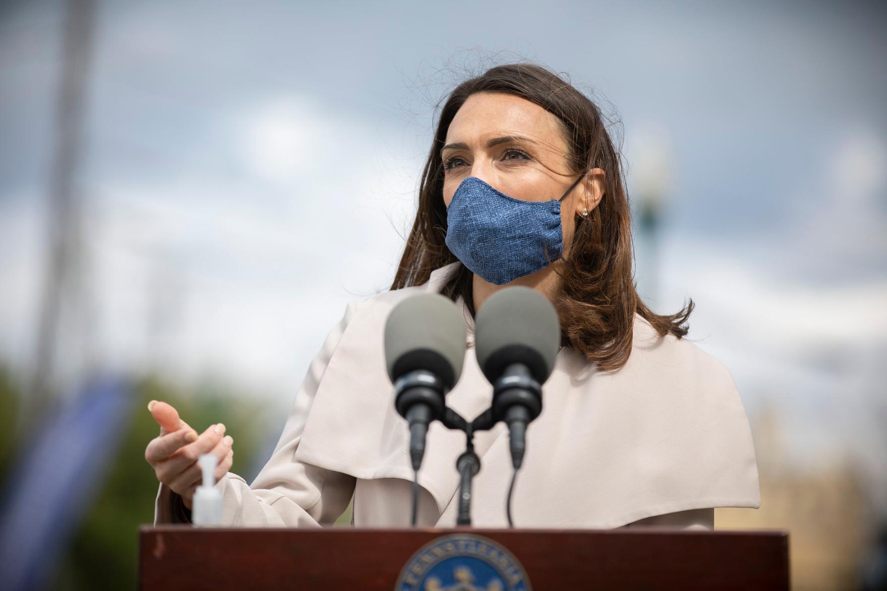 Alison Beam wears a mask while speaking from a podium.