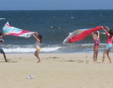 Children play with beach towels on a windy day in Belmar, N.J., on Tuesday. Millions are expected to hit the road or board a plane to celebrate Memorial Day weekend as more people get vaccinated and COVID-19 restrictions are scaled back. (Wayne Parry/AP Photo)