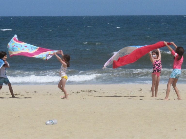 Children play with beach towels on a windy day in Belmar, N.J., on Tuesday. Millions are expected to hit the road or board a plane to celebrate Memorial Day weekend as more people get vaccinated and COVID-19 restrictions are scaled back. (Wayne Parry/AP Photo)