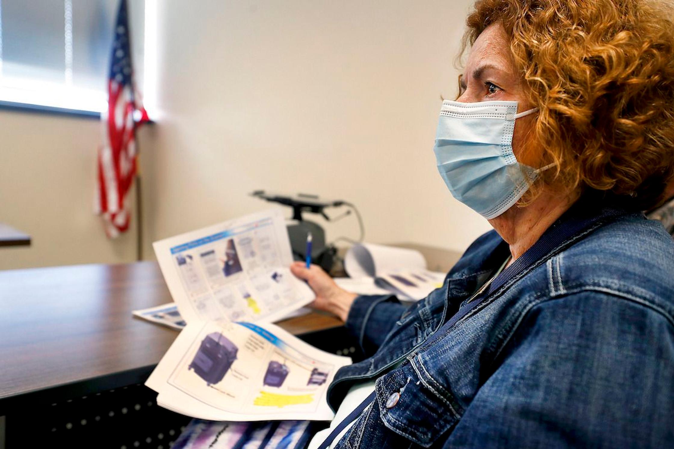 An election official sits with paperwork while wearing a face mask