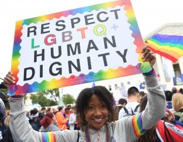 A person holds up a rainbow sign that says 