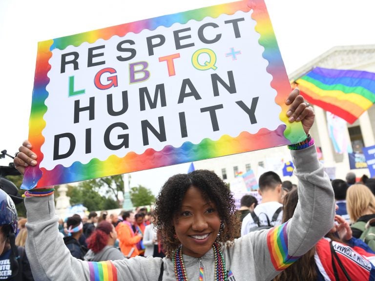 A person holds up a rainbow sign that says 