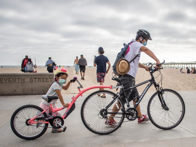 A girl and her father wear face masks while they push their bikes in Hermosa Beach