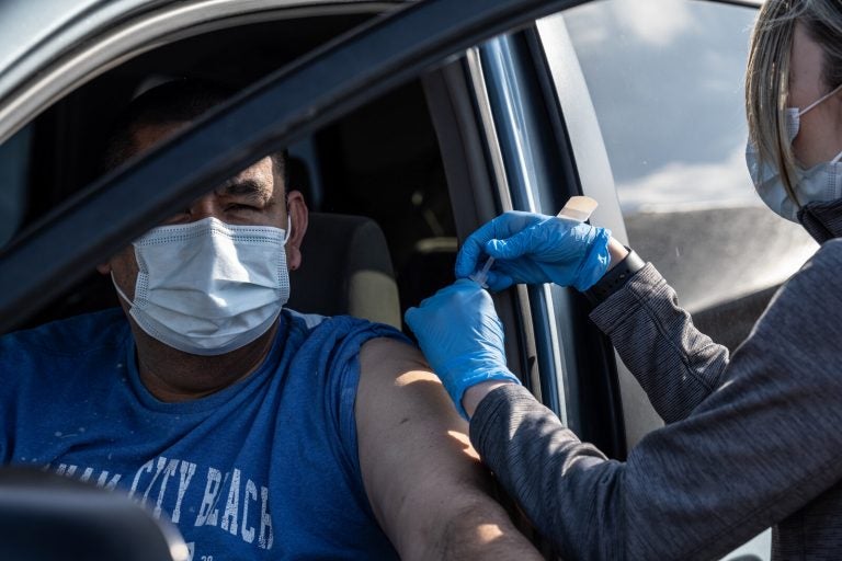 A medical professional from UofL Health administers a vaccine to a patient in their vehicle