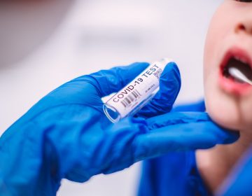 A doctor’s hands in protection gloves putting COVID-19 test swab into kid’s mouth